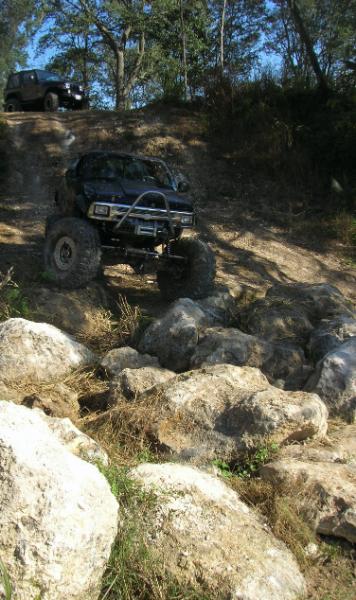 1989 Ford Bronco - Two off-road vehicles navigating a challenging rocky trail on a sunny day.