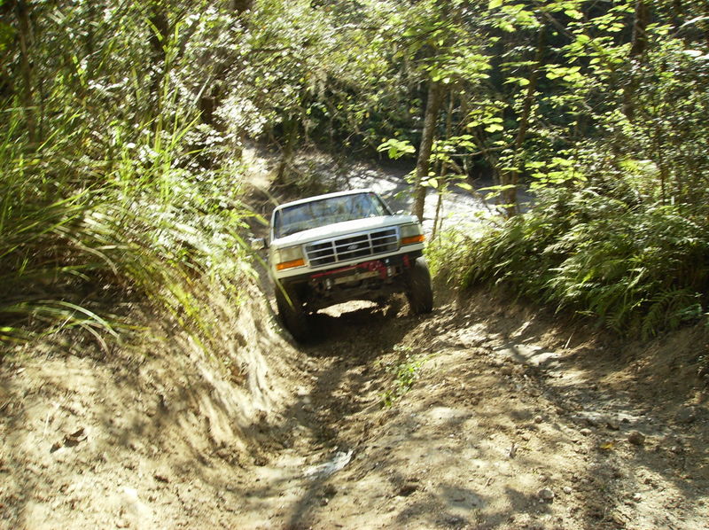 White Ford Bronco driving off-road on a muddy trail, front 3/4 view