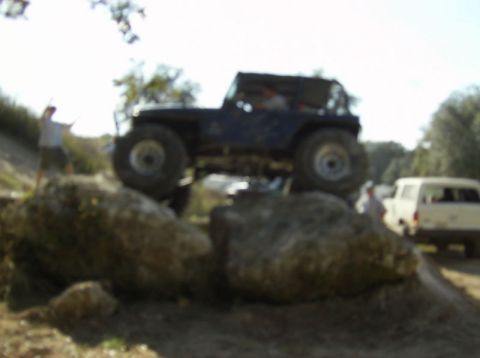 1989 Ford Bronco - A dark blue off-road vehicle navigates a rocky terrain, with another vehicle visible in the background.