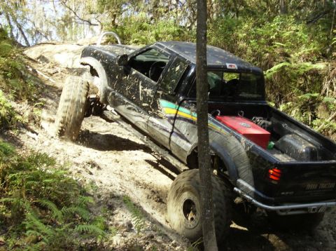 1989 Ford Bronco - This modified pickup truck is navigating a challenging off-road course with significant mud and incline.