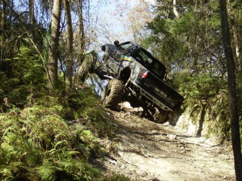 1989 Ford Bronco - A black pickup truck navigates a challenging off-road course through a wooded area.