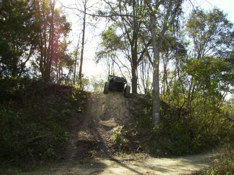 1989 Ford Bronco - An off-road vehicle navigates a challenging incline on a dirt path surrounded by trees.