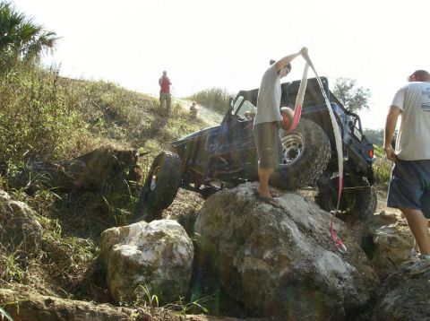 1989 Ford Bronco - A modified off-road vehicle is being maneuvered over large rocks with assistance from bystanders.