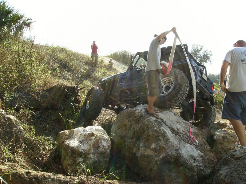 Off-road vehicle navigating rocky terrain with people assisting