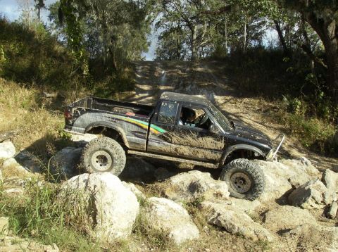 1989 Ford Bronco - This pickup truck is covered in mud as it drives over large rocks on an off-road trail.