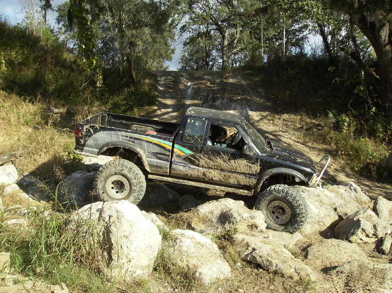 Muddy black pickup truck with large tires navigating a rocky, off-road trail