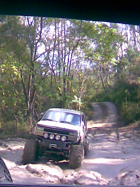 1989 Ford Bronco - This modified SUV navigates a rough, wooded trail with large tires and auxiliary lights.