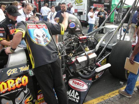 1998 Ford Crown Victoria - crew member in a Skull Shine shirt tends to the supercharged engine of a black Torco-sponsored top fuel dragster in the pits.