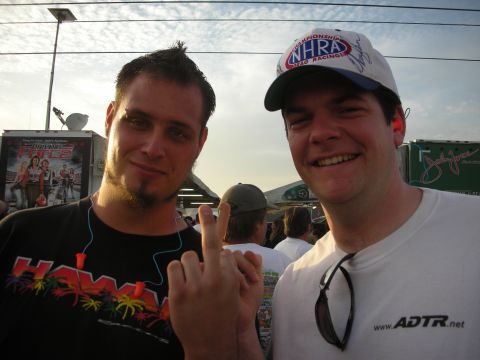 1998 Ford Crown Victoria - Two young men pose together at an outdoor racing event, one wearing an NHRA hat at dusk.