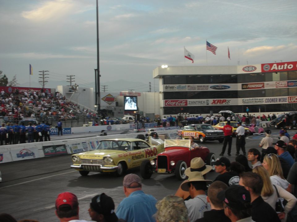 Yellow gasser and a red hot rod roadster at the starting line before a crowd