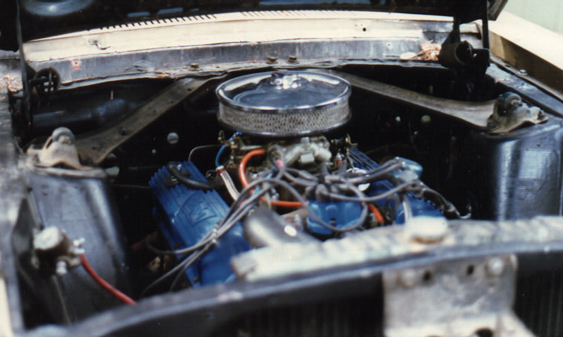 Engine bay with V8, blue valve covers, chrome air cleaner and carburetor in black-painted compartment