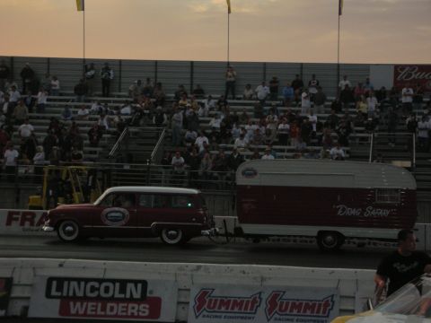 1998 Ford Crown Victoria - maroon vintage station wagon tows a matching trailer lettered "Drag Safari" along the track at sunset.