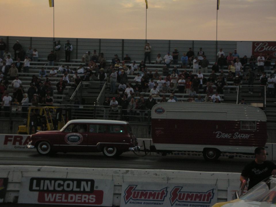 Maroon vintage station wagon towing a matching teardrop-style trailer on track