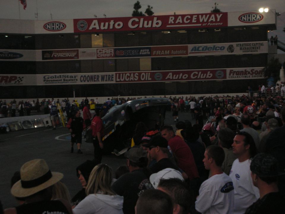 Crowd watching a funny car at Auto Club Raceway at Pomona in low light