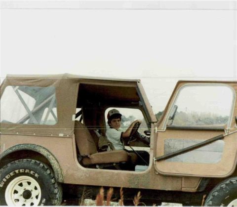 1994 Ford Bronco - A child sits behind the wheel of a brown Jeep CJ-7, with the driver's side door open.