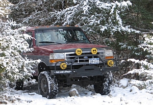 1986 Ford Bronco - 1992 Ford Bronco navigating a snowy forest trail with aftermarket modifications.