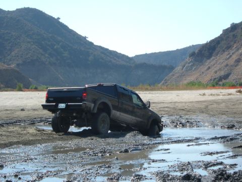 1981 Ford Bronco - Pickup truck is stuck in a muddy area with hills in the distance.