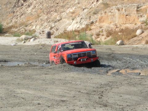 1981 Ford Bronco - An off-road vehicle navigates a muddy terrain, with a website sticker visible on its windshield.