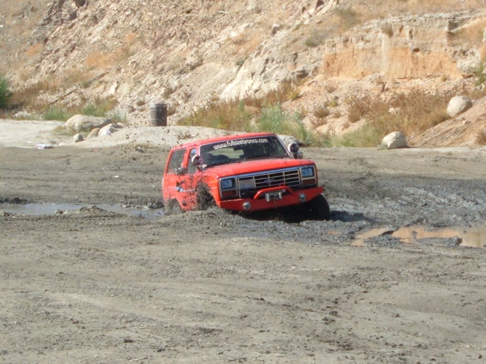 Red SUV stuck in mud, has 'www.fullsizebronco.com' sticker on windshield