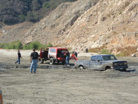 1981 Ford Bronco - Two off-road vehicles are stuck in the mud at an outdoor site with a rocky hillside in the background.