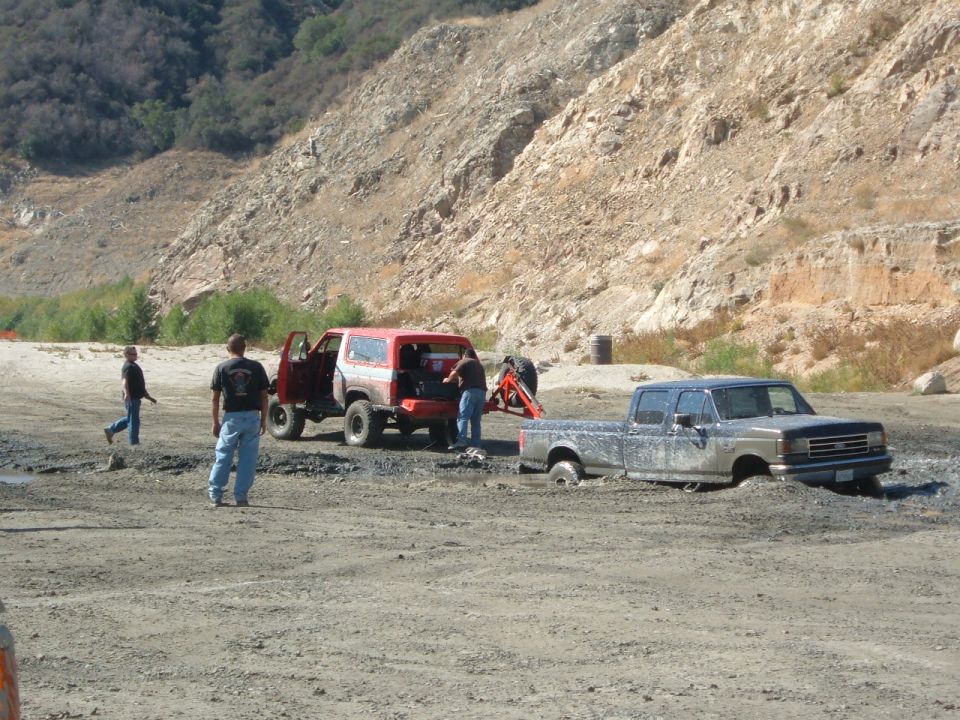 Red 1981 Ford Bronco and stuck pickup truck in mud