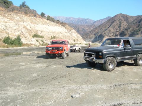 1981 Ford Bronco - Several off-road vehicles are parked in a dusty, mountainous area under a clear blue sky.