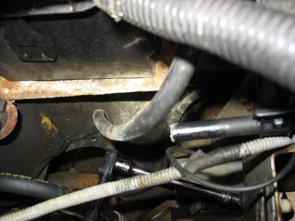 Close-up of engine bay showing hoses, wiring, and a socket wrench on a bolt