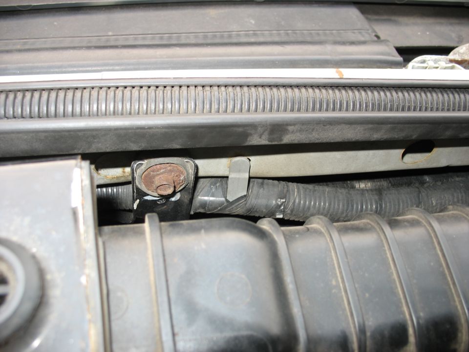 Engine bay part with rusted bolt and black hose