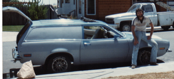 Light blue Ford Pinto wagon, side view with rear hatch open, man leaning on front fender at curb