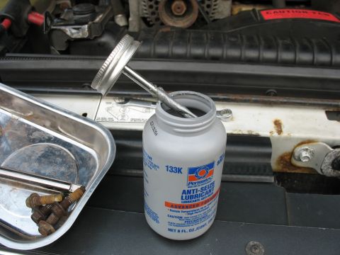 1995 Ford C-350 (Centurion Conversions) - A bottle of anti-seize lubricant sits next to a tray of bolts in an engine bay.