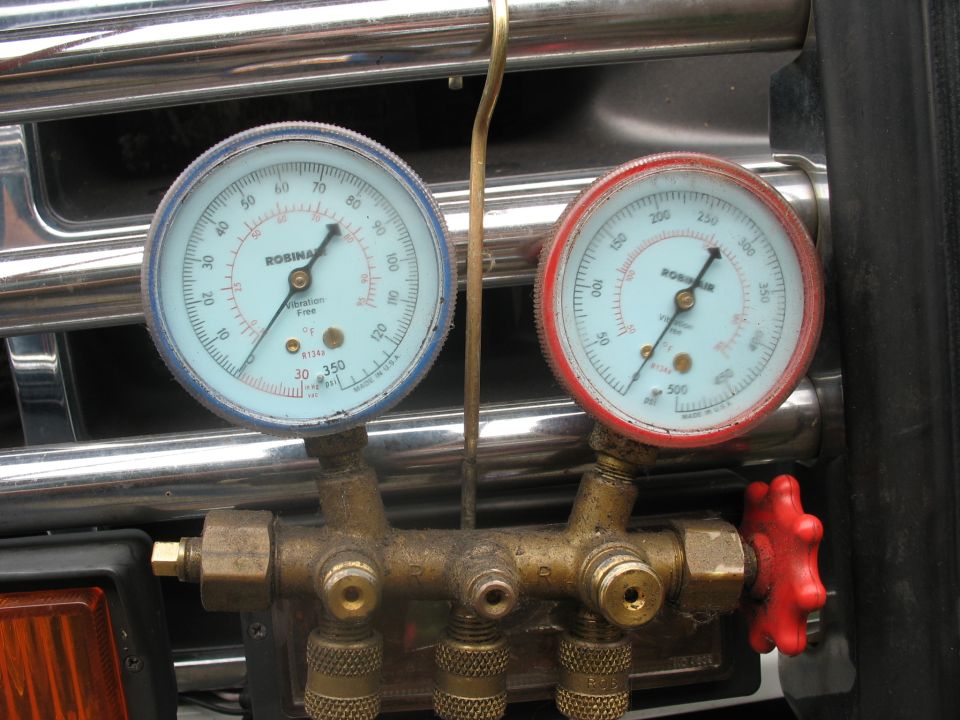 AC manifold gauge set with blue and red gauges mounted in front of a chrome grille