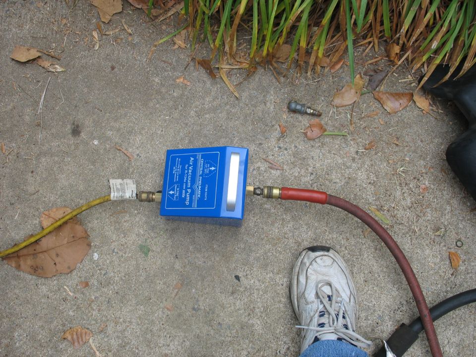 Blue air vacuum pump connected to hoses, with a person's shoe and jeans visible