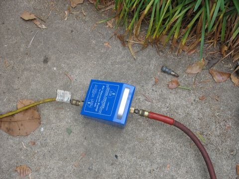1995 Ford C-350 (Centurion Conversions) - A blue air vacuum pump is connected to hoses on a concrete surface with scattered leaves and grass.