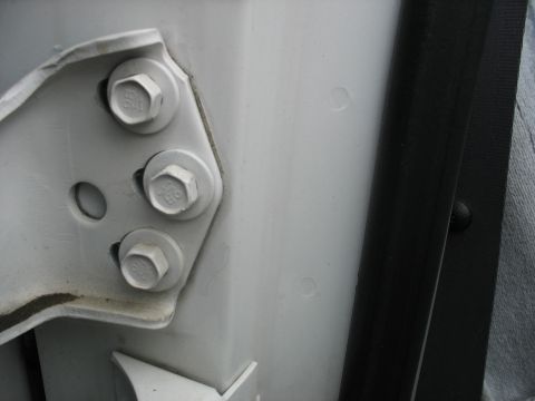1995 Ford C-350 (Centurion Conversions) - Close-up of a vehicle's door hinge and frame, showing the mounting hardware and a rubber seal.