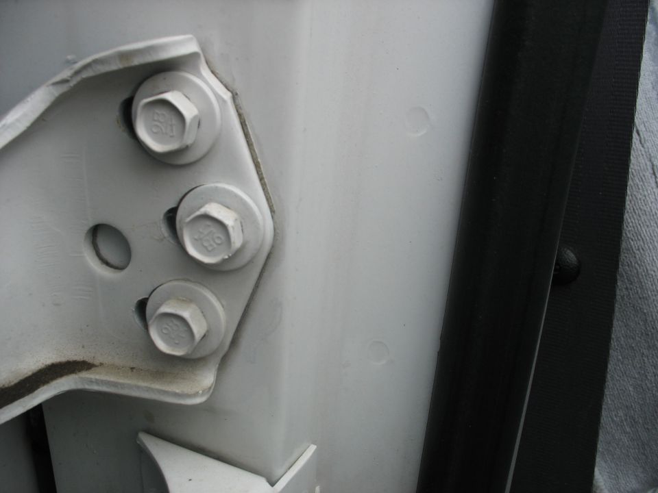 White door hinge with three bolts attached to a white frame. Black rubber seal visible