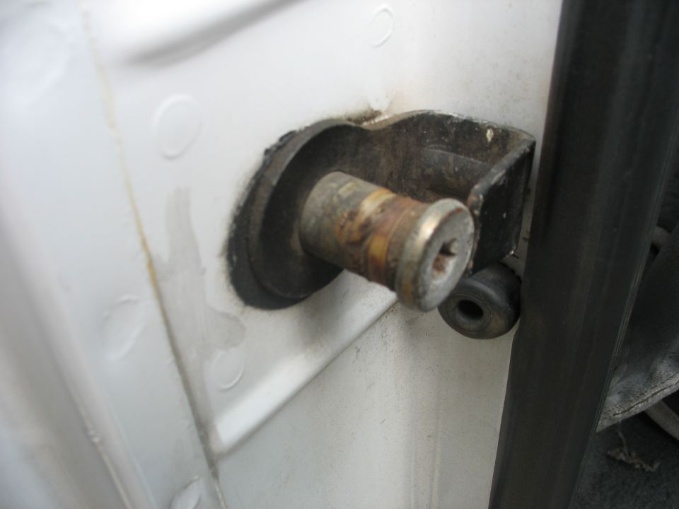Close-up of a rusted door hinge pin on a white vehicle body
