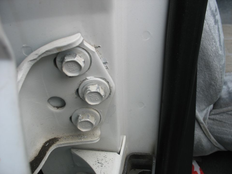 Close-up of three white bolts on a vehicle's door hinge mechanism