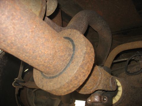 1995 Ford C-350 (Centurion Conversions) - Close-up view of rusted driveshaft and exhaust system components underneath a vehicle.
