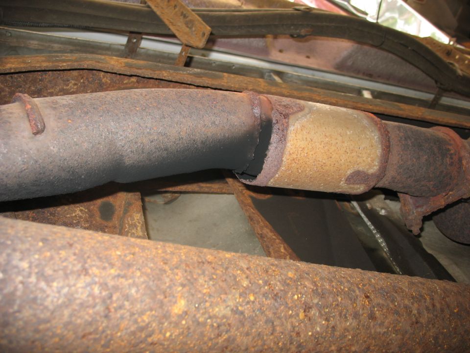 Close-up of rusted exhaust pipe and catalytic converter under a vehicle
