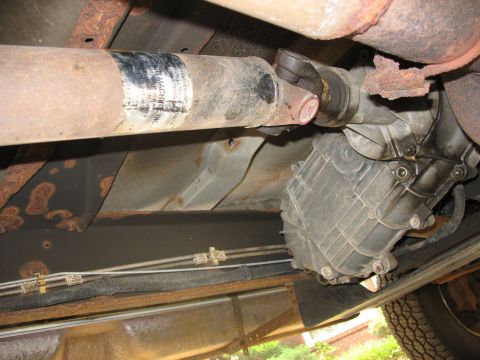 1995 Ford C-350 (Centurion Conversions) - Underside view of a vehicle's driveshaft and transfer case, showing signs of age and corrosion.