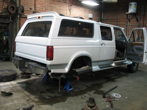 1995 Ford C-350 (Centurion Conversions) - White van conversion undergoing repairs in a garage, with its wheels off and doors open.