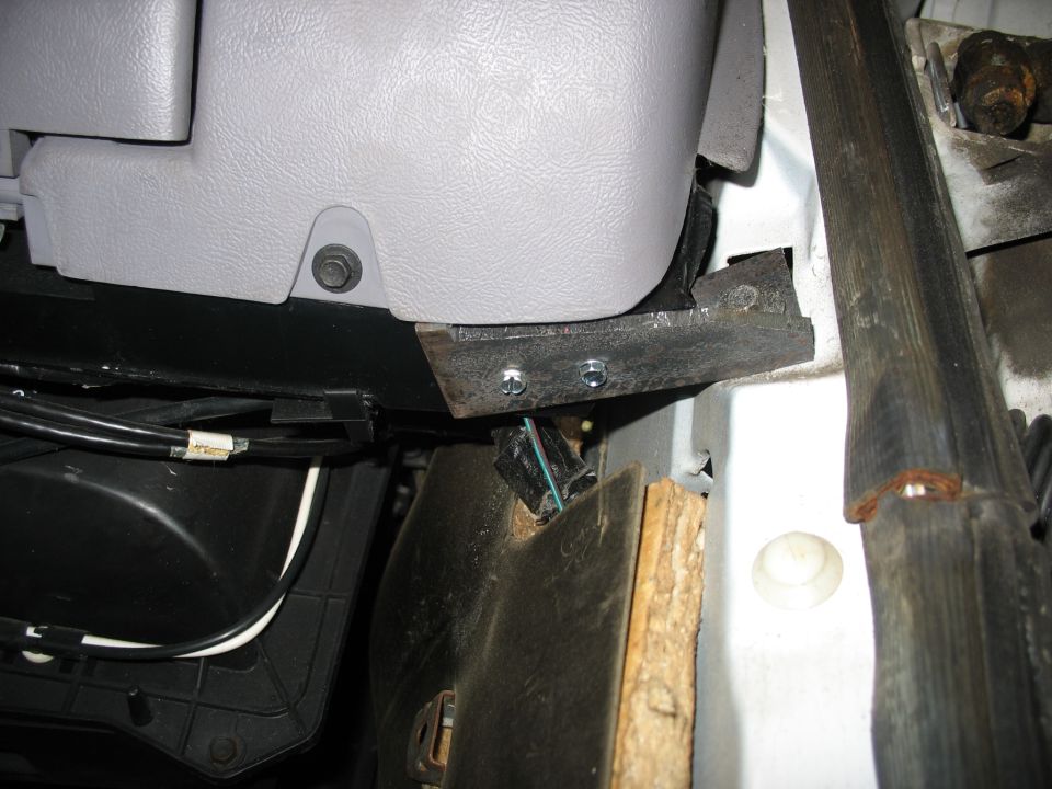 Gray plastic dashboard trim secured with bolts to a metal bracket, with wiring visible below