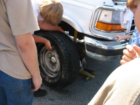 1995 Ford C-350 (Centurion Conversions) - A group of people work together to change a flat tire on a white truck.