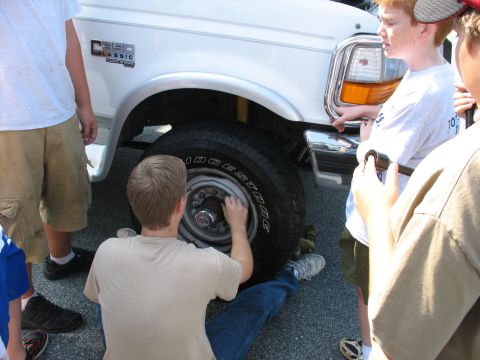 1995 Ford C-350 (Centurion Conversions) - A group of people, likely Boy Scouts, work on the front wheel of a white 1995 Ford C-350 (Centurion Conversions) truck.