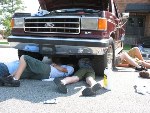 1995 Ford C-350 (Centurion Conversions) - Several individuals are lying on the ground, working on the underside of a maroon Ford truck.