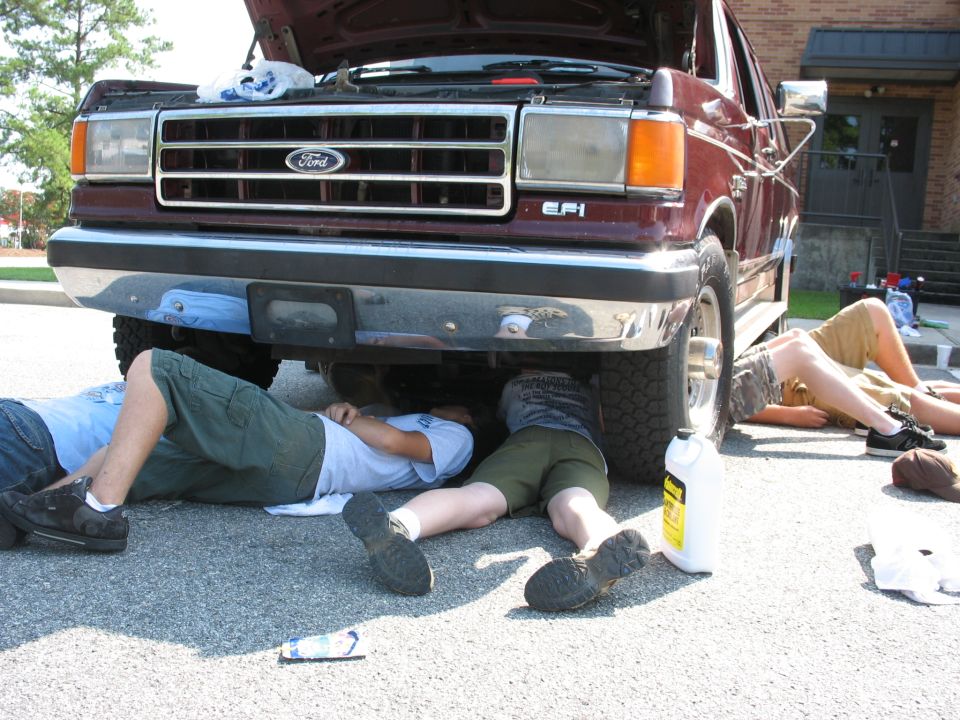 People working under a maroon Ford truck. The grille has a Ford logo