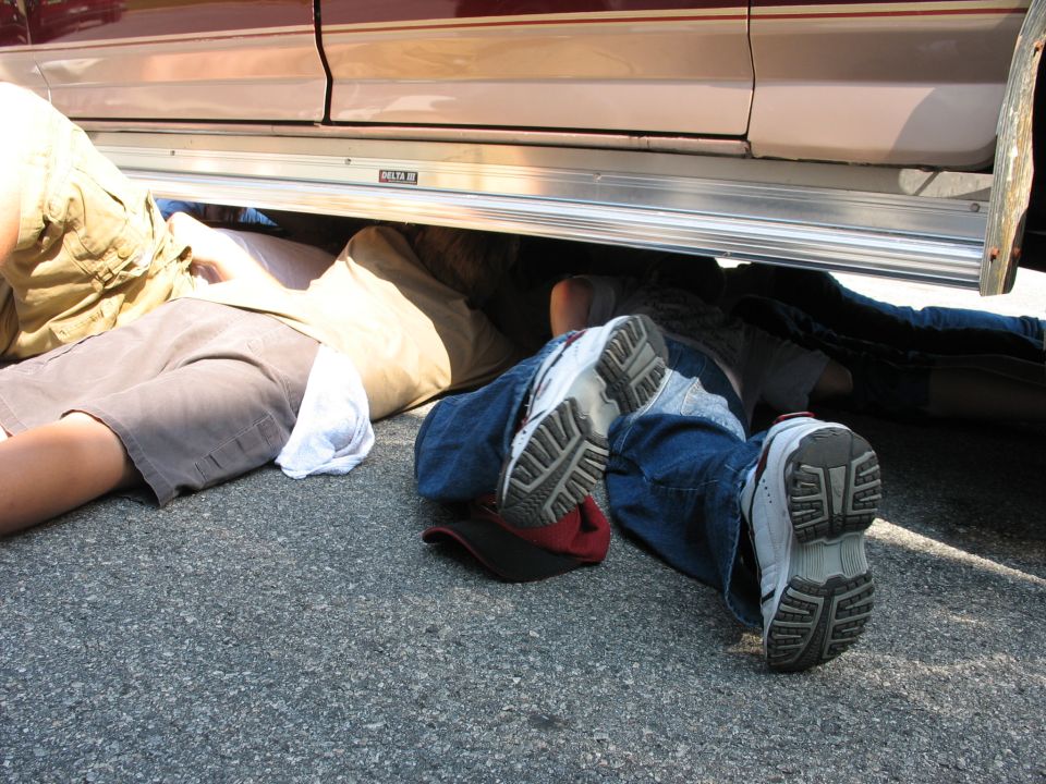 Several people are lying on the ground underneath a vehicle, with their legs and feet visible