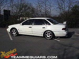 1993 Ford Taurus - White 1993 Ford Taurus sedan with aftermarket wheels and a small spoiler is parked in a lot.