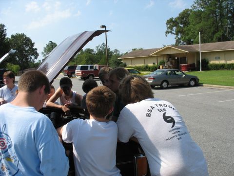 1995 Ford C-350 (Centurion Conversions) - A group of individuals, possibly Boy Scouts, examine the engine compartment of a vehicle outdoors.