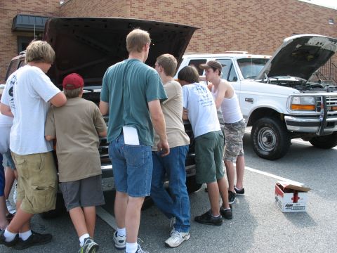 1995 Ford C-350 (Centurion Conversions) - A group of boys inspect the engine bay of a white Ford F-Series truck.